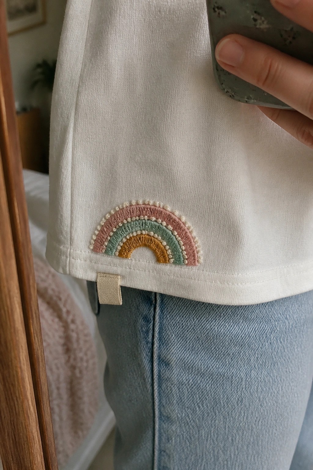 White t-shirt sleeve with pastel rainbow embroidery above blue jeans
