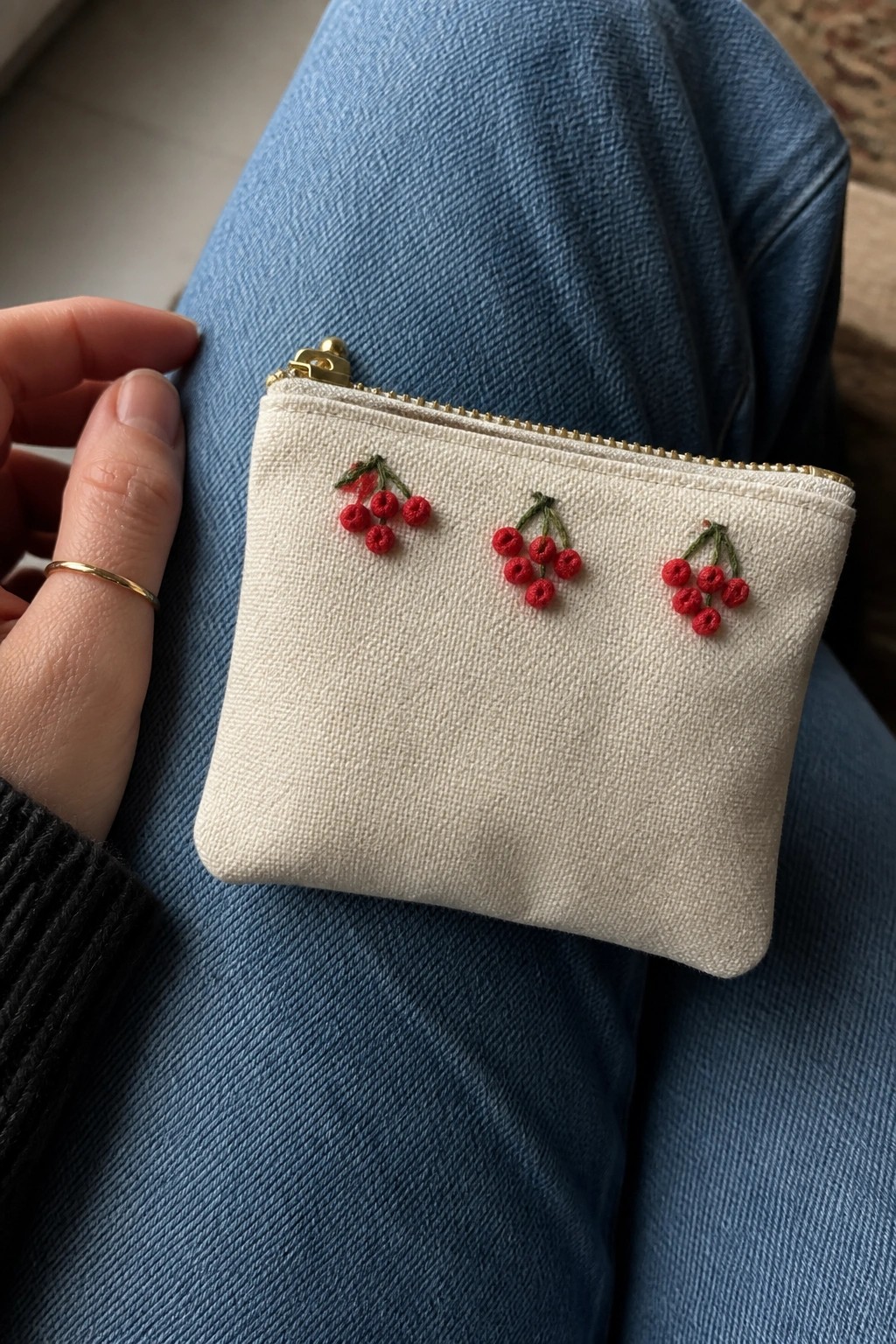 White zippered pouch with red cherry embroidery on blue denim jeans
