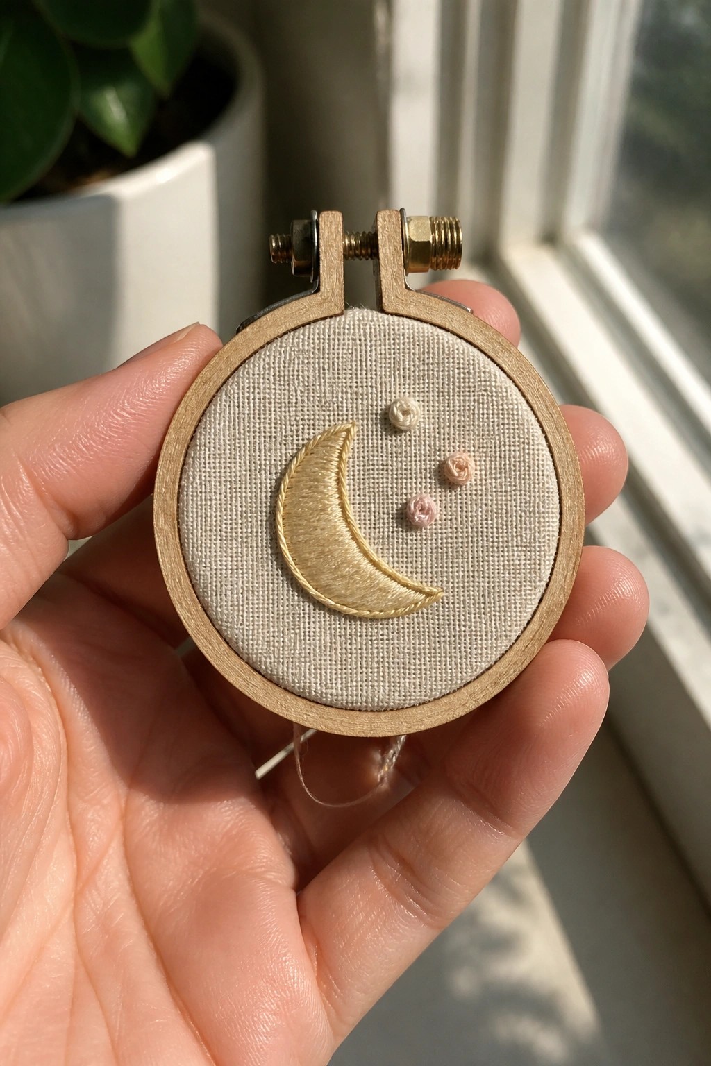 Hand holding wooden hoop with gold crescent moon and three small pink flowers