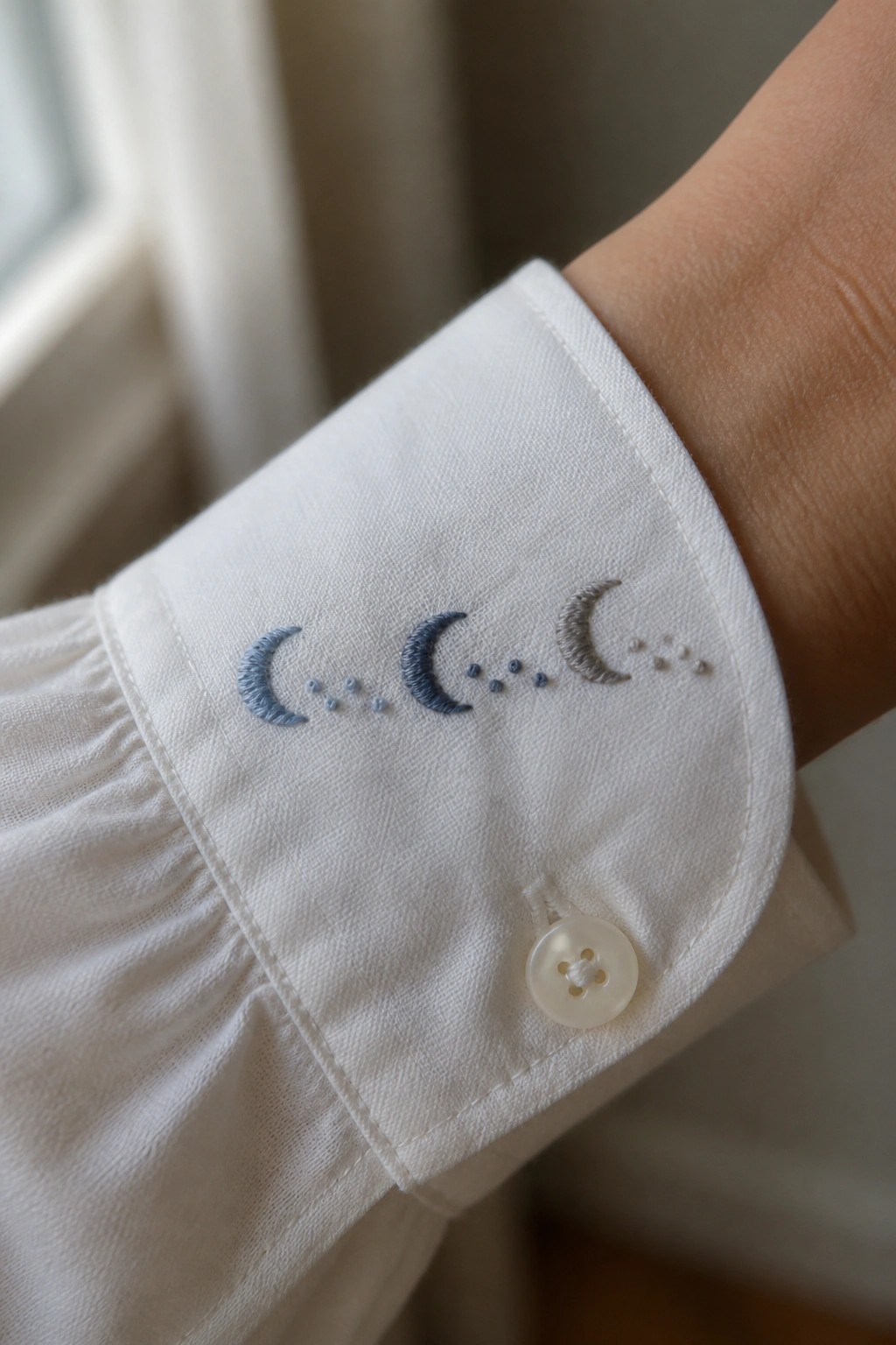 White shirt cuff embroidered with blue-gray crescent moons and dots, button attached.