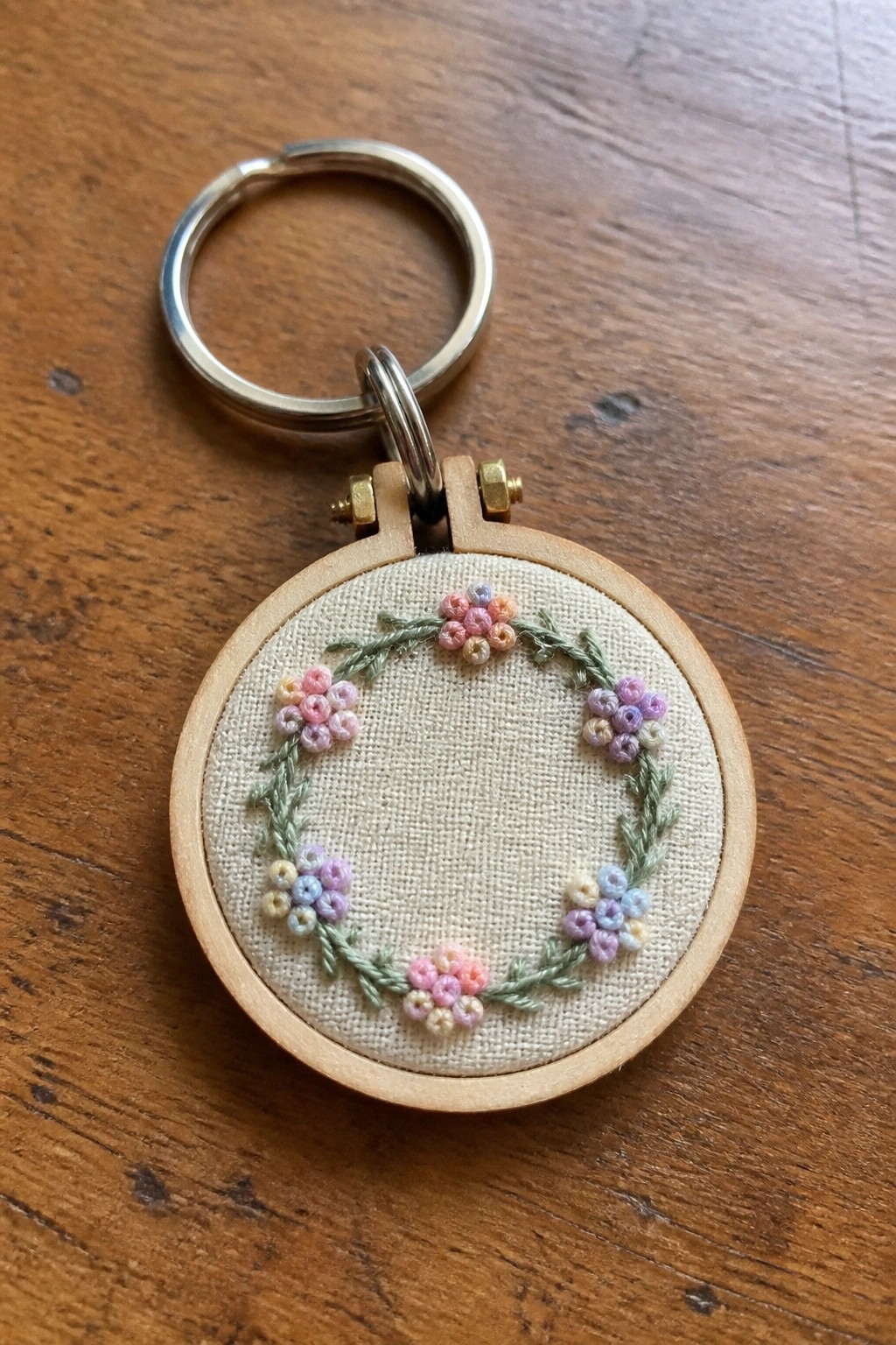 Miniature wooden embroidery hoop keychain with pastel floral wreath on beige fabric
