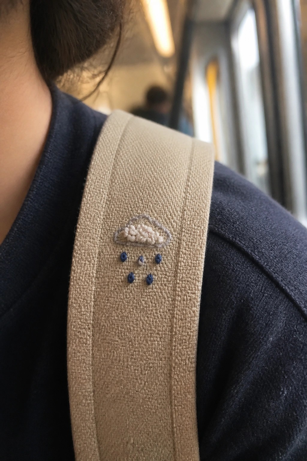 A beige fabric strap with an embroidered cloud and scattered blue raindrop knots.