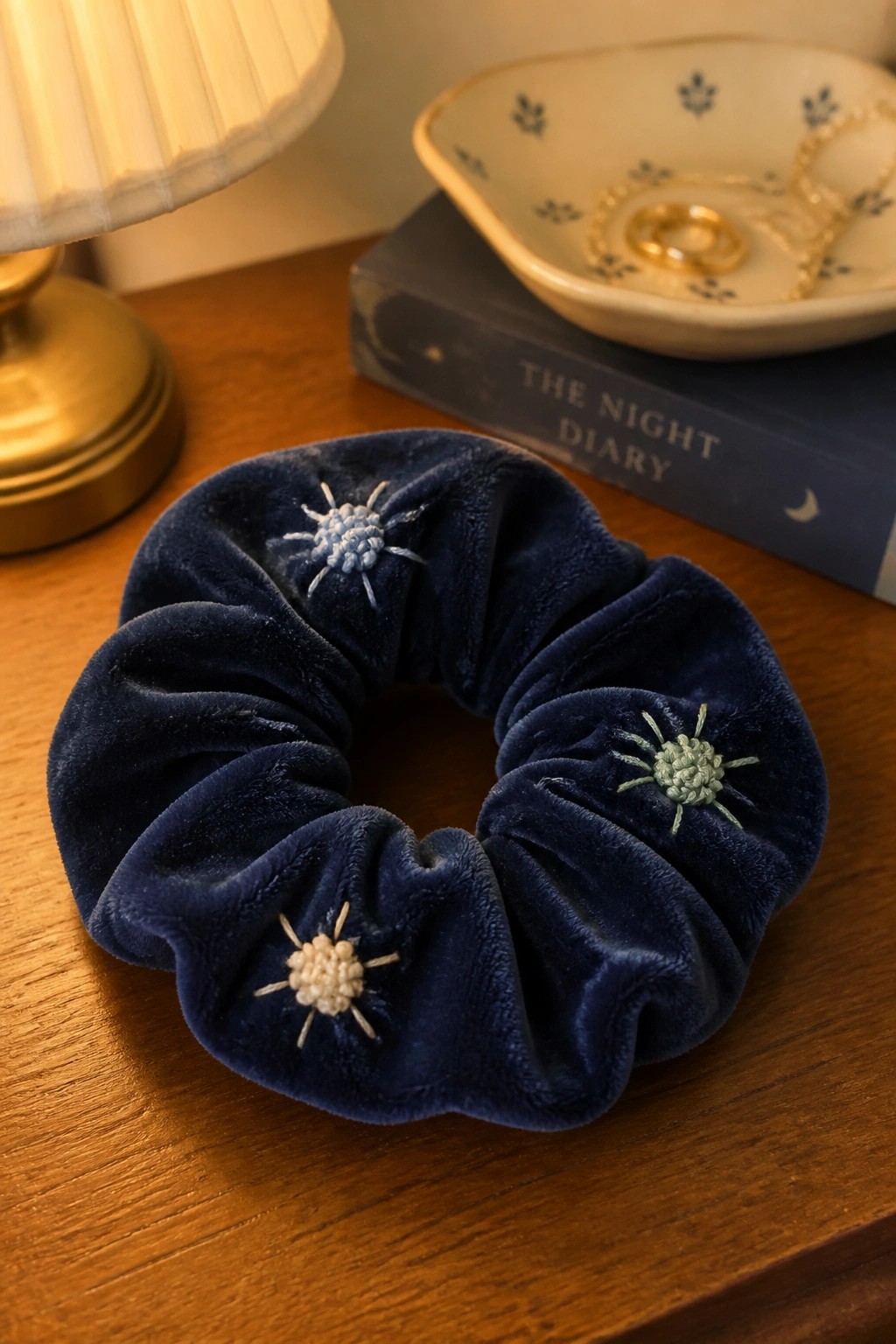 Navy blue velvet scrunchie with three pastel embroidered sun designs on wood table