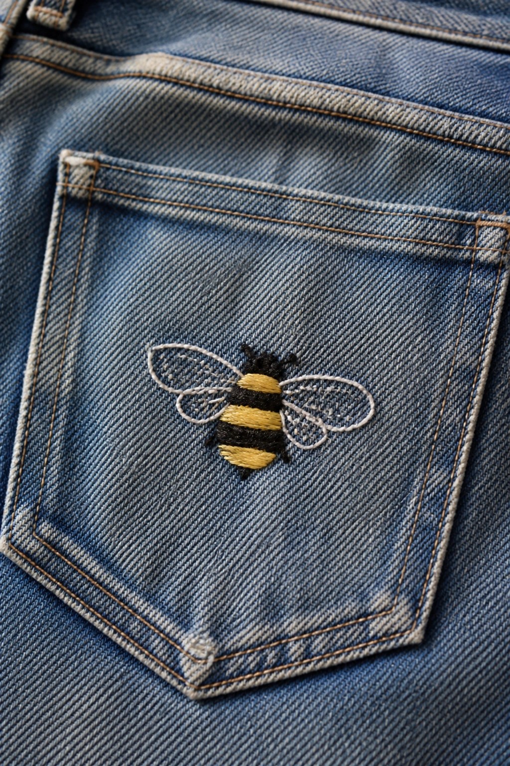 A bee embroidered on a blue denim jeans pocket.