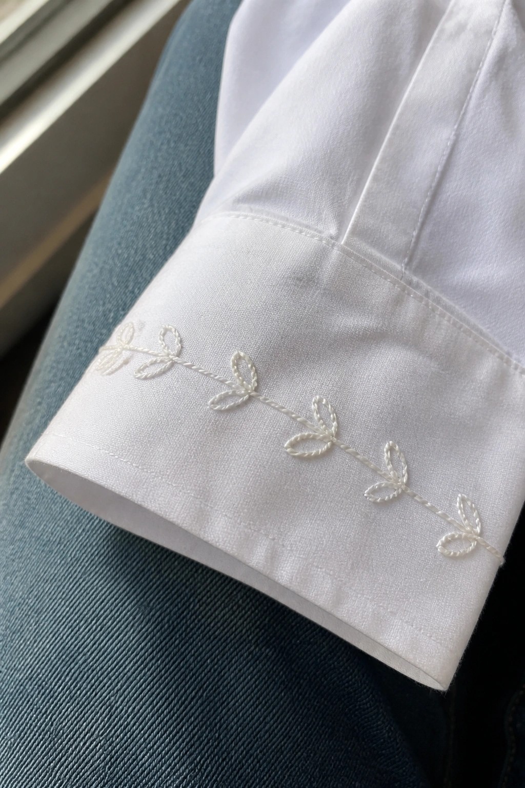 White embroidery of a vine with small loops along the edge of a white shirt cuff.
