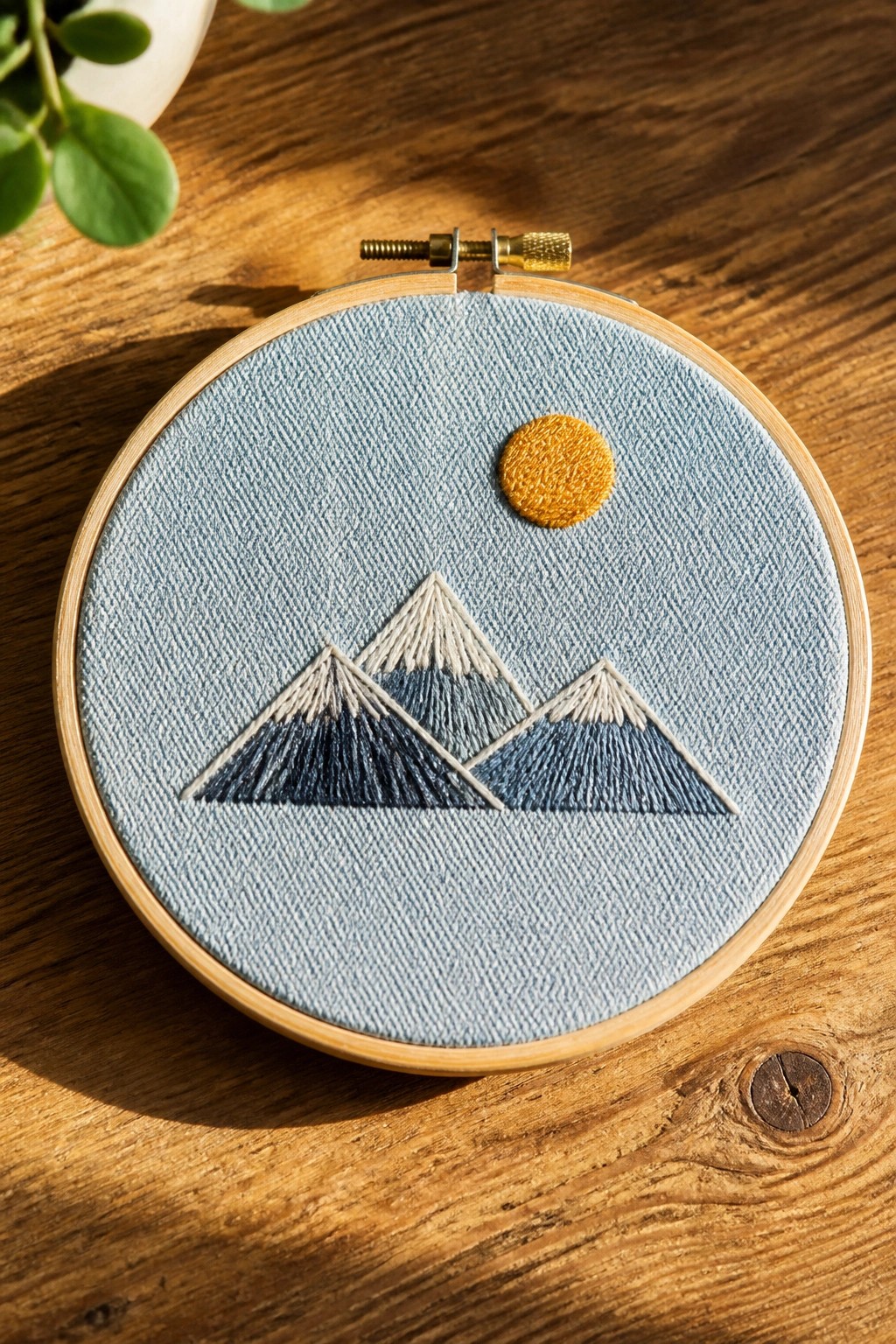 Embroidery hoop with blue mountain peaks and yellow sun on wooden table