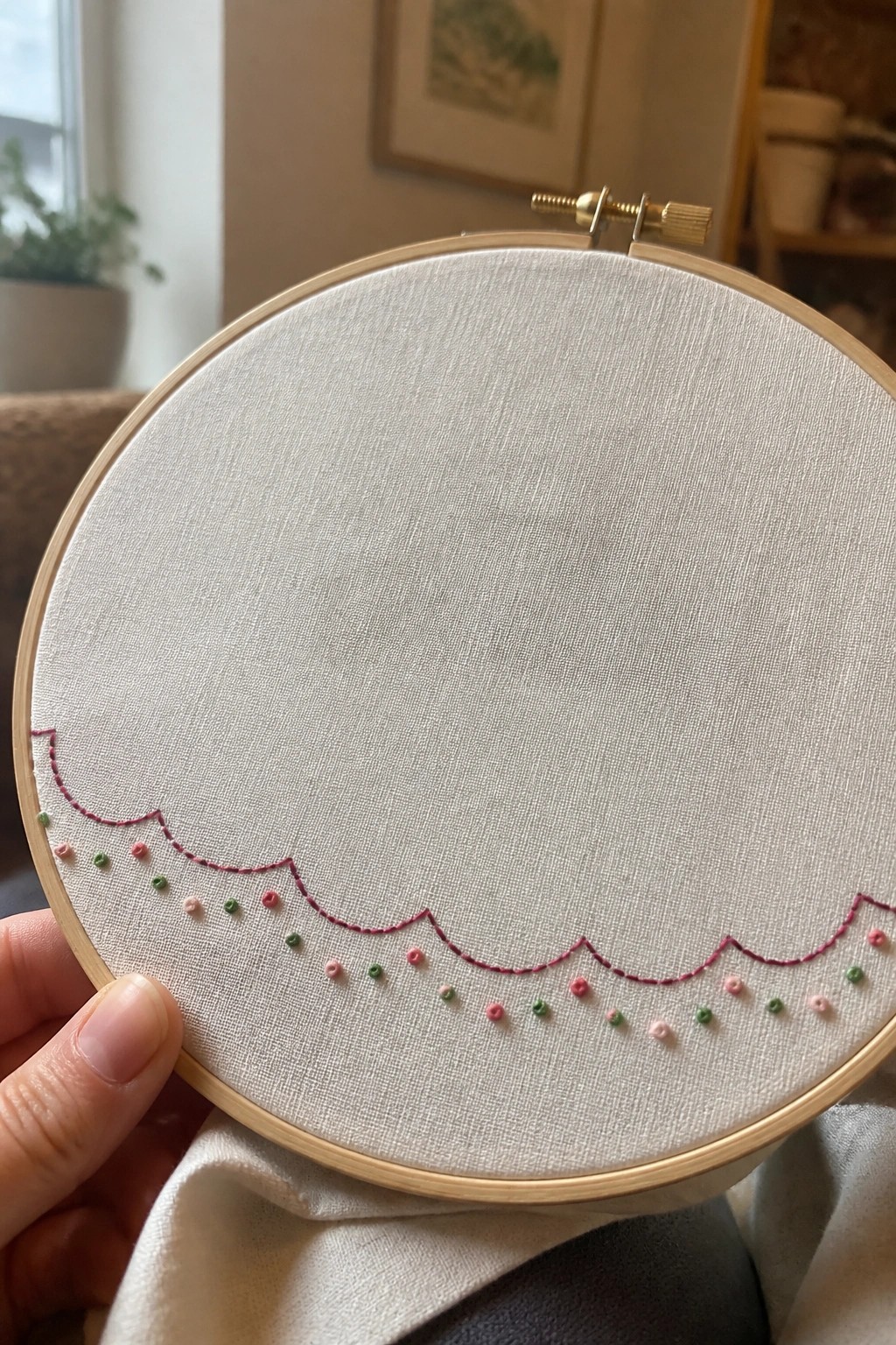Hand holding embroidery hoop with pink scalloped stitches and pink green dots on fabric