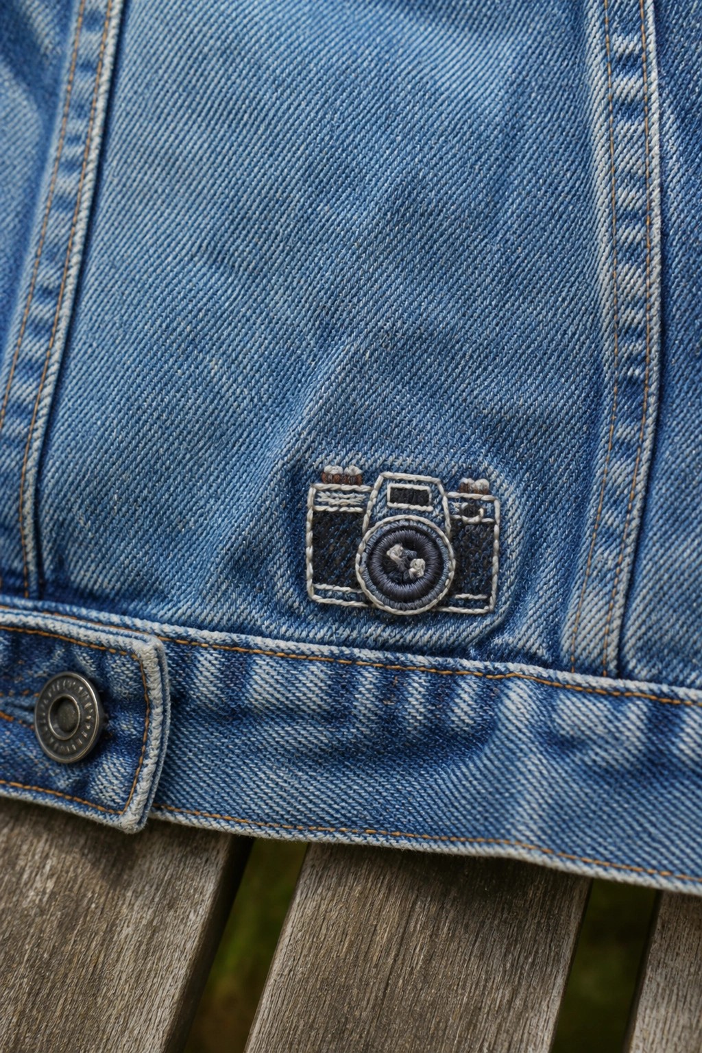 Blue denim jacket with embroidered camera patch and metal button on wood
