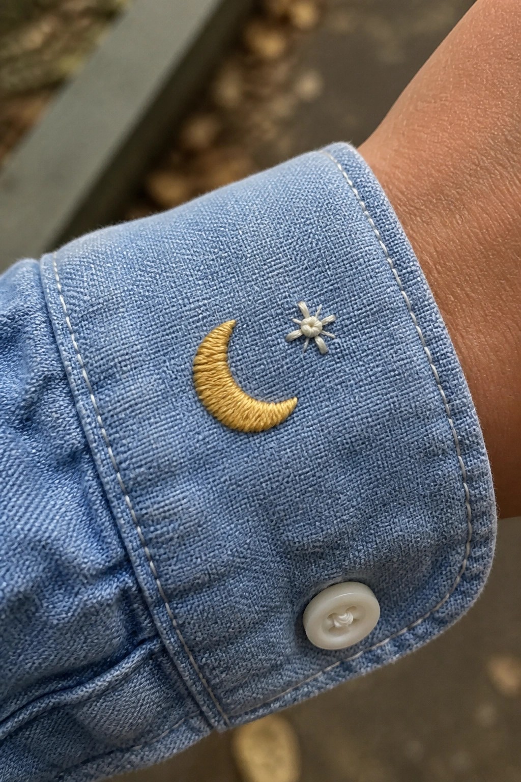 Blue denim shirt cuff with yellow crescent moon, white star embroidery, and button.
