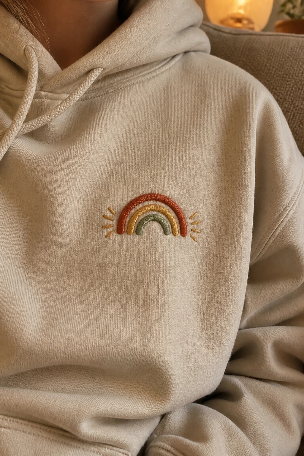 Beige hoodie with embroidered rainbow in terracotta, yellow and green tones.