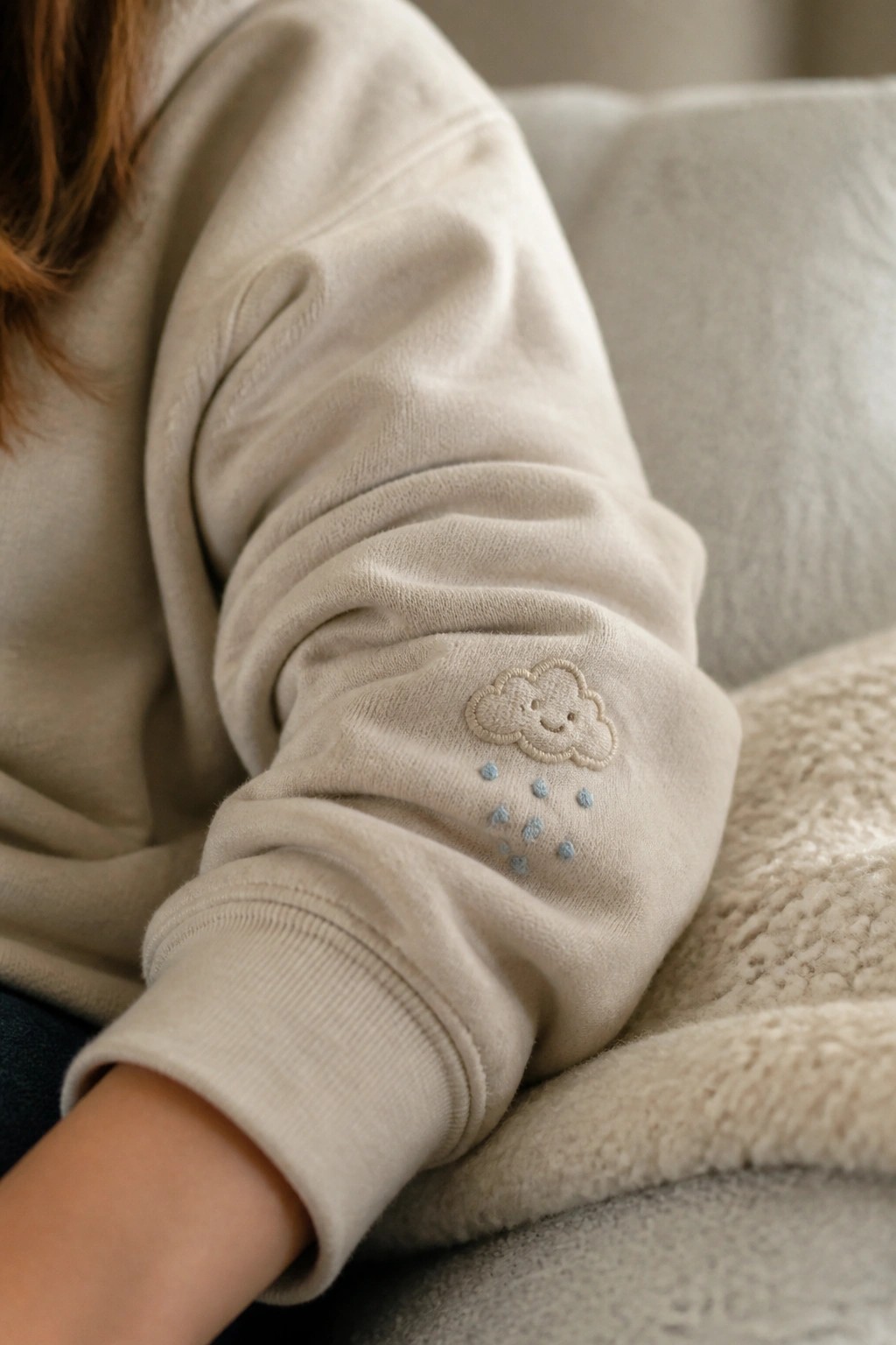 Cream sweatshirt sleeve with embroidered smiling cloud and blue raindrops on arm