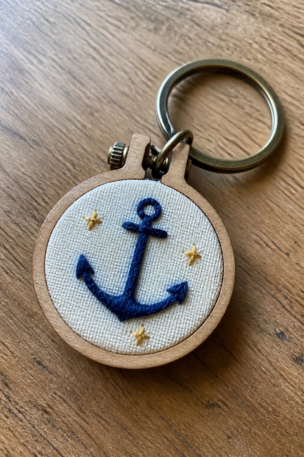 Miniature wooden embroidery hoop keychain with blue anchor and gold stars.