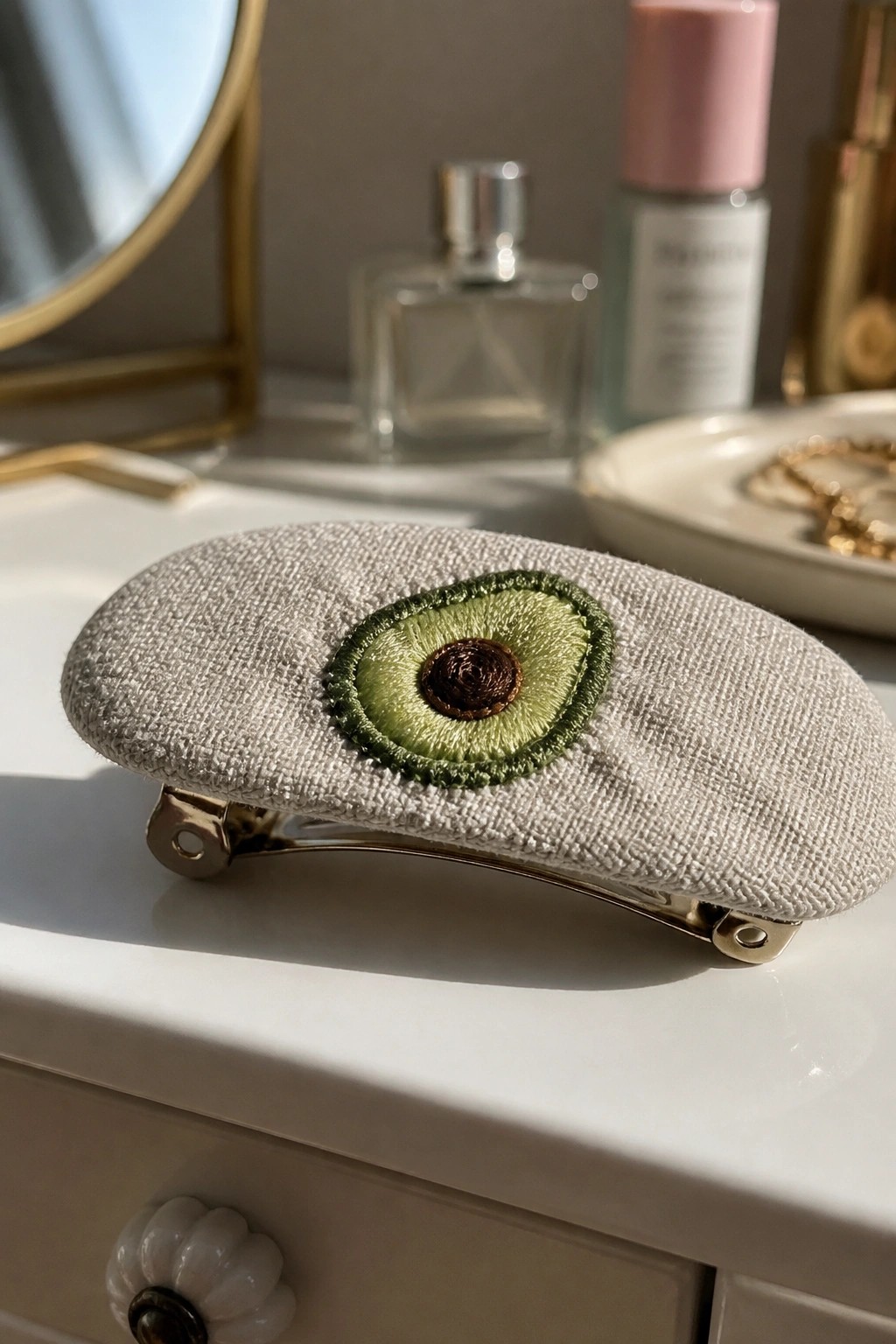 Linen hair clip with embroidered avocado on white vanity amid cosmetics.