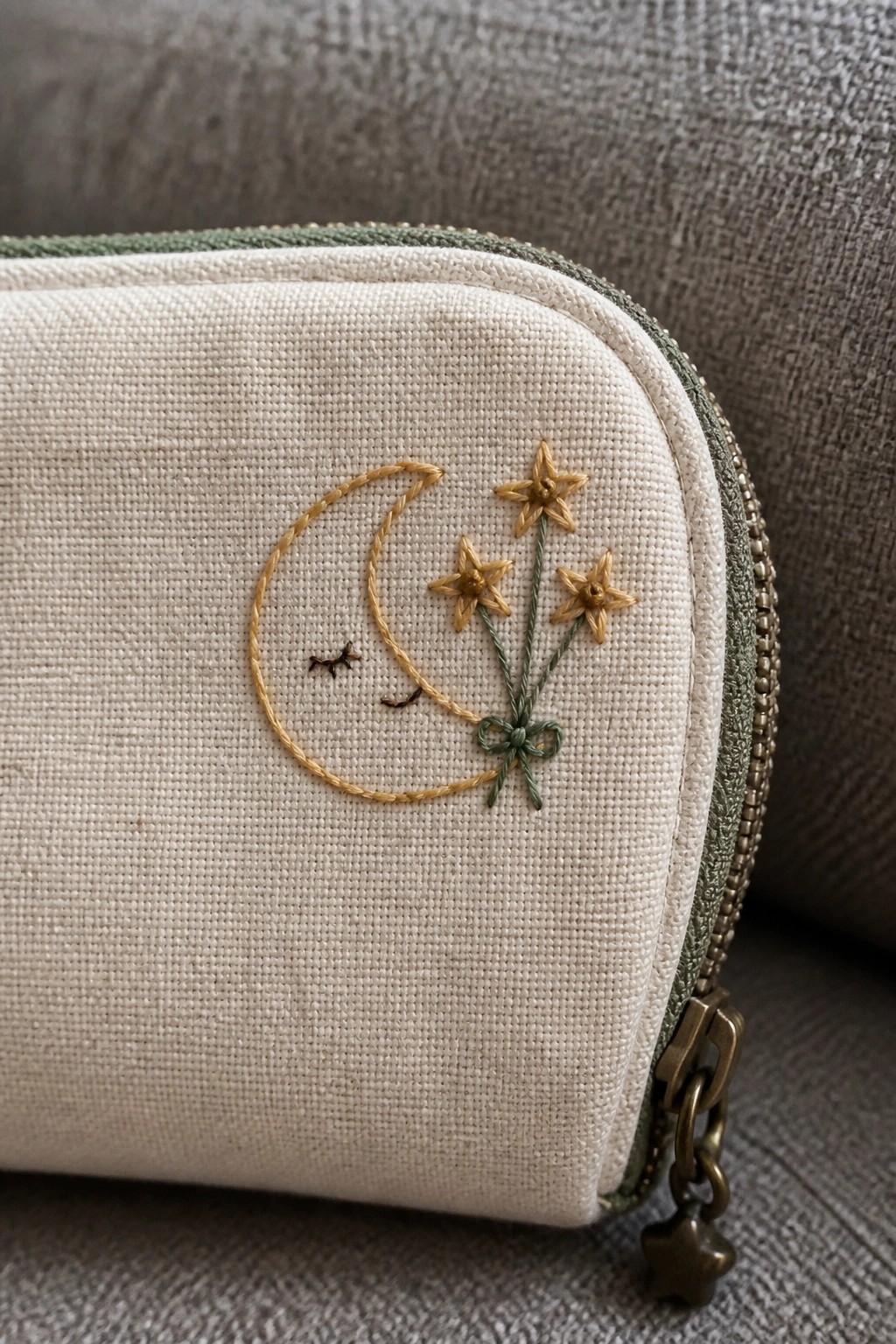Cream zippered pouch with yellow crescent moon, sleeping face, three yellow star flowers on green stems, and green bow embroidery.
