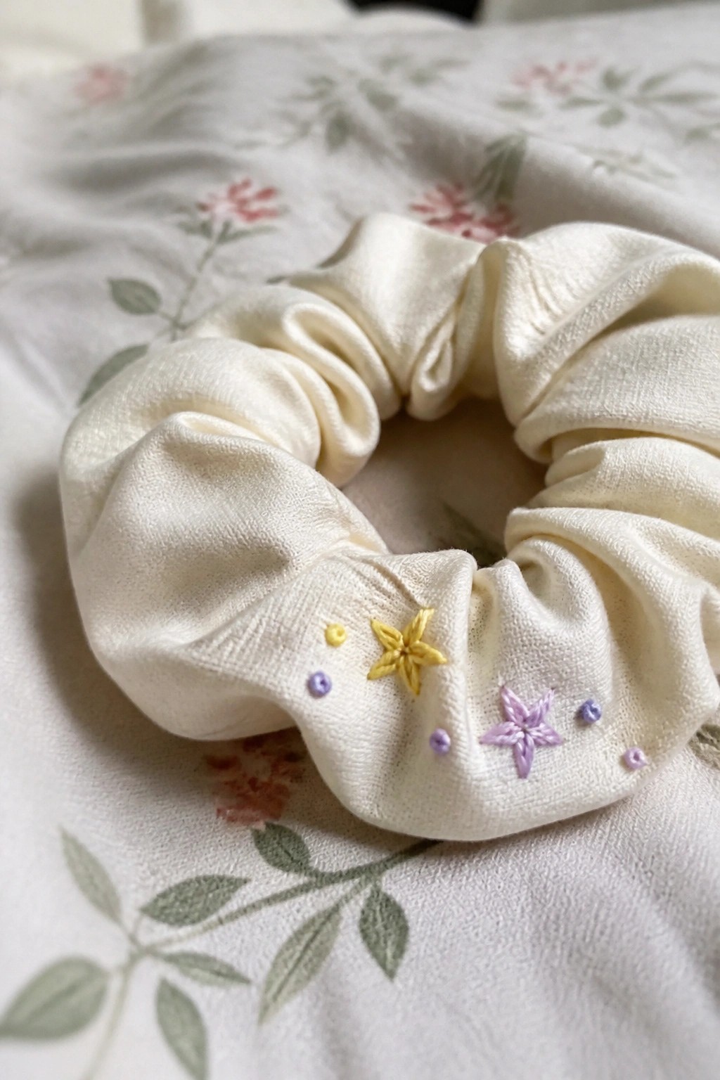 White scrunchie with yellow and purple embroidered stars on floral fabric