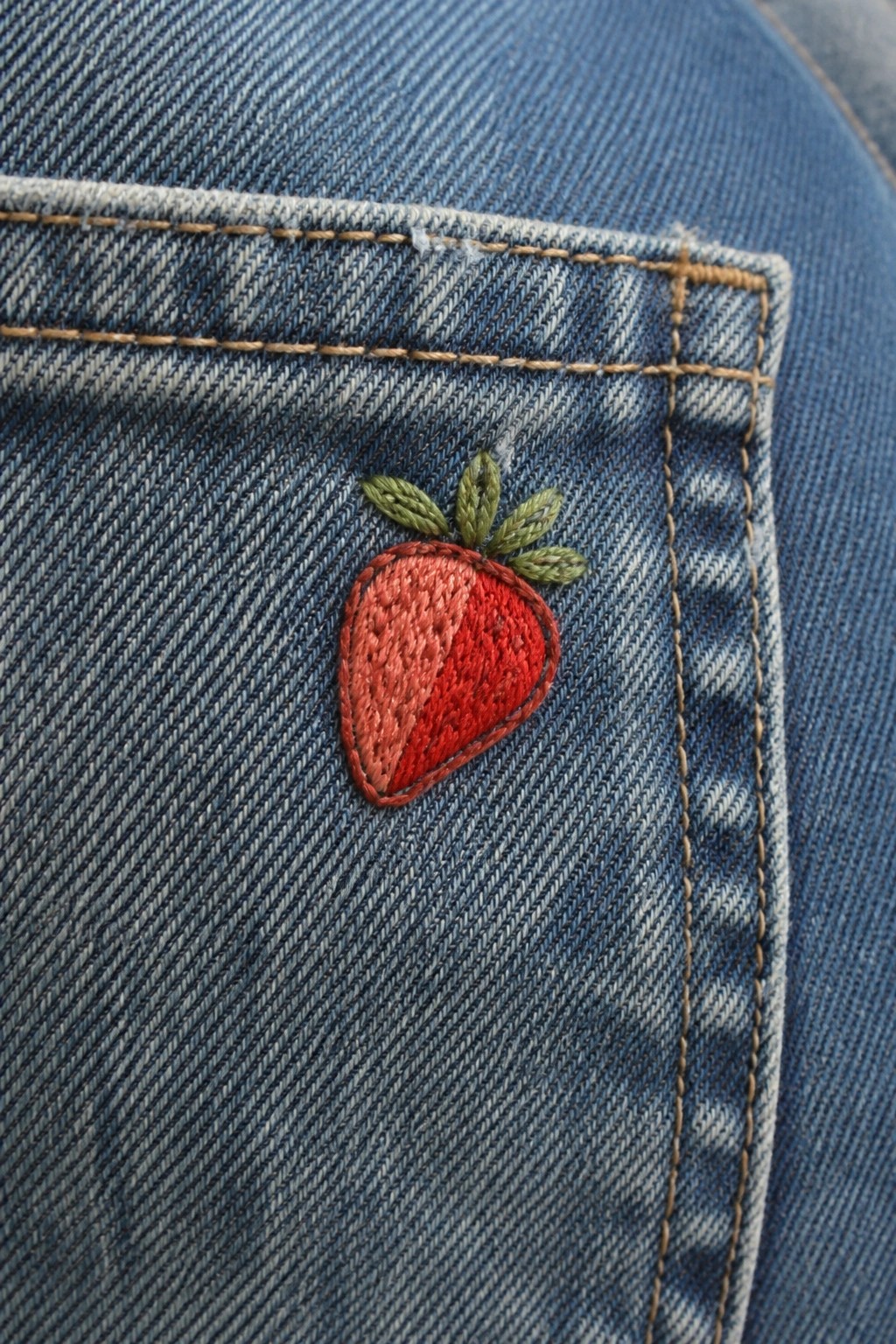 Blue denim jeans pocket with red embroidered strawberry and green leaves