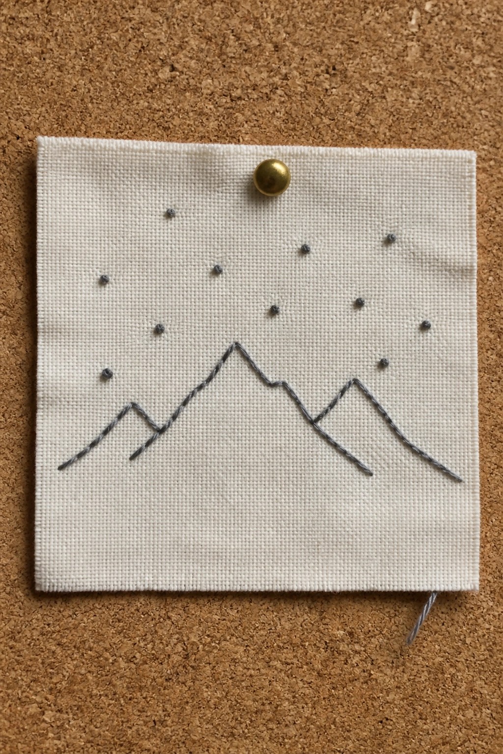 Square of white fabric with gray embroidered mountain peaks and scattered dots pinned to corkboard.