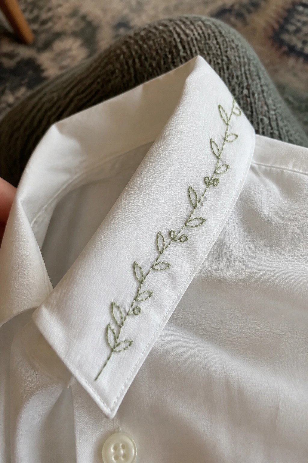 White shirt collar with delicate green vine and leaf embroidery above button.