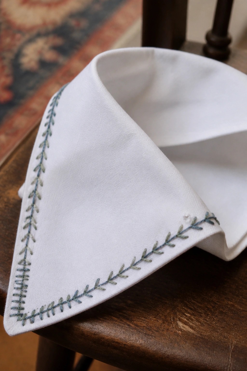 White fabric with blue-green embroidered leaf edges on dark wooden surface