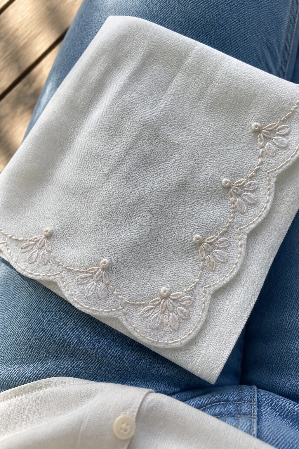 White embroidered shirt cuff with scalloped floral design on blue denim jeans.