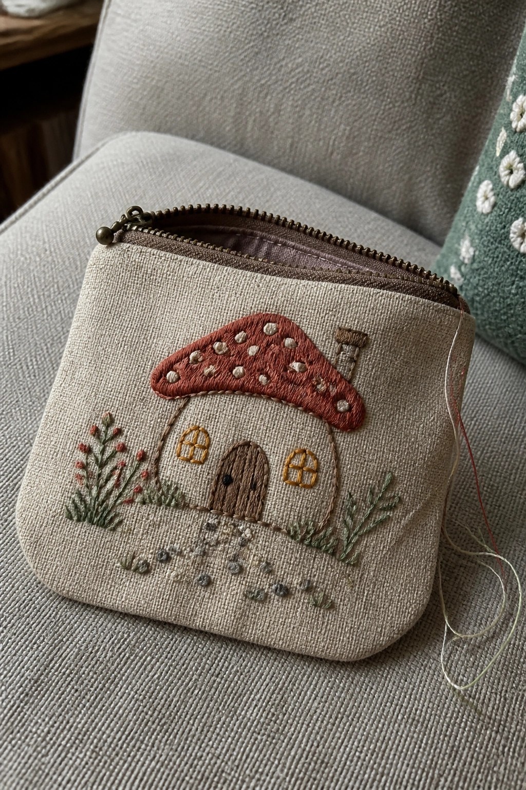 Beige zippered pouch embroidered with red mushroom house, door, and plants