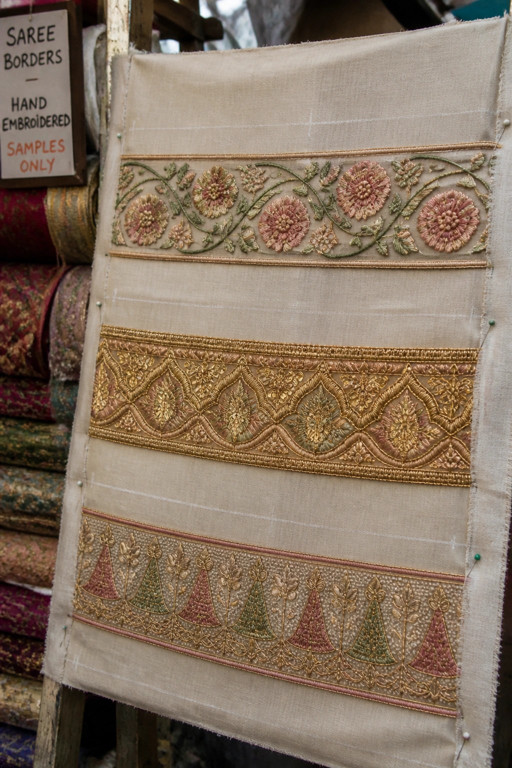 Hand-embroidered saree borders with floral and geometric patterns on beige fabric.