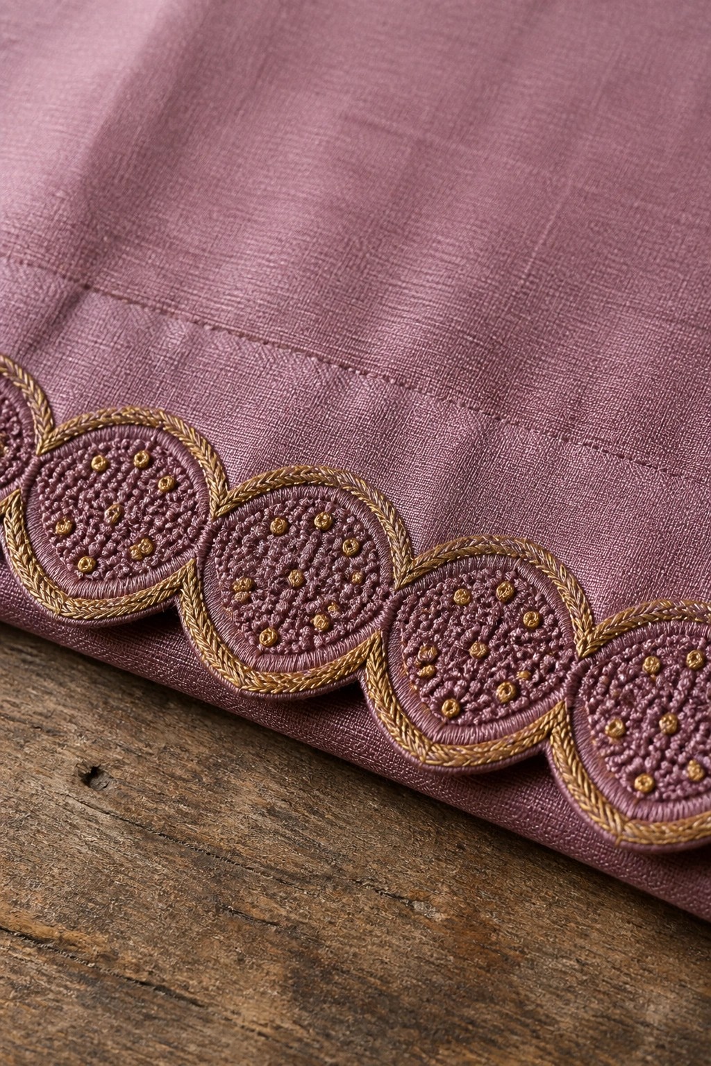 Mauve fabric with scalloped gold-outlined circular embroidery on wooden surface