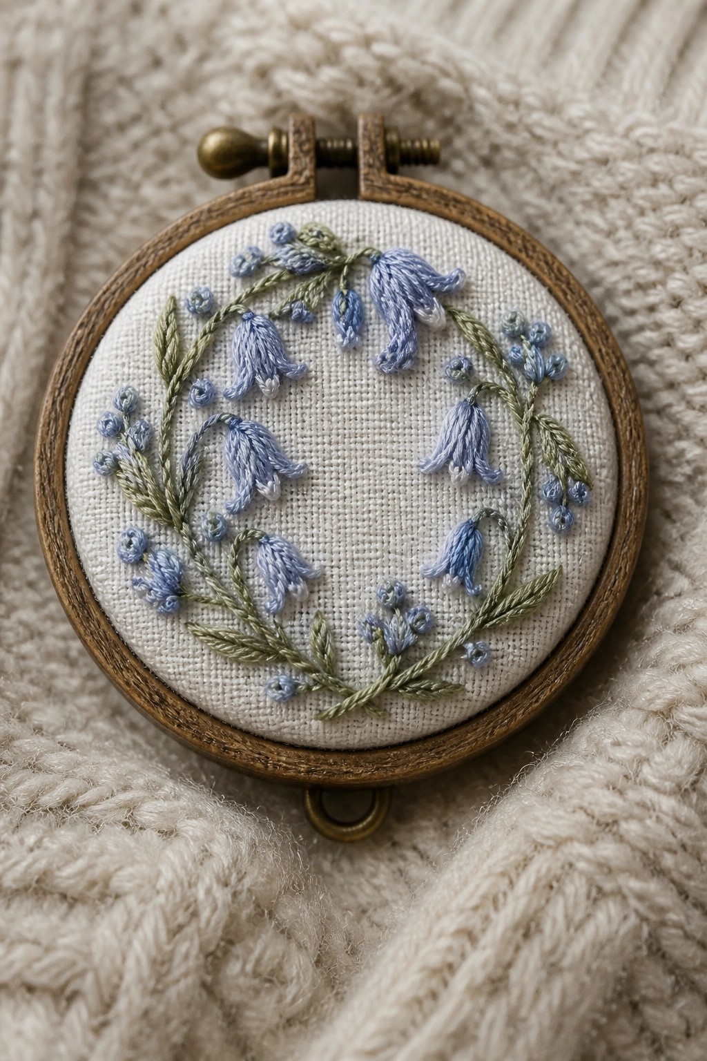 Wooden hoop with bluebell embroidery on white fabric over beige knit.