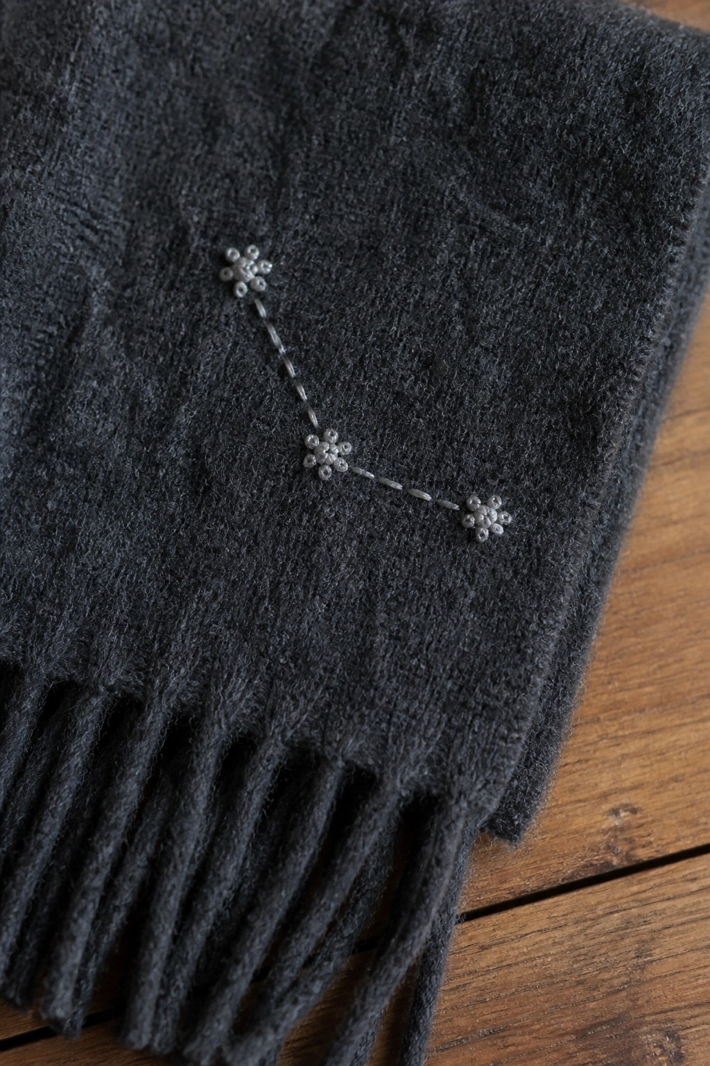 Dark gray fringed scarf with silver beaded constellation embroidery on wood