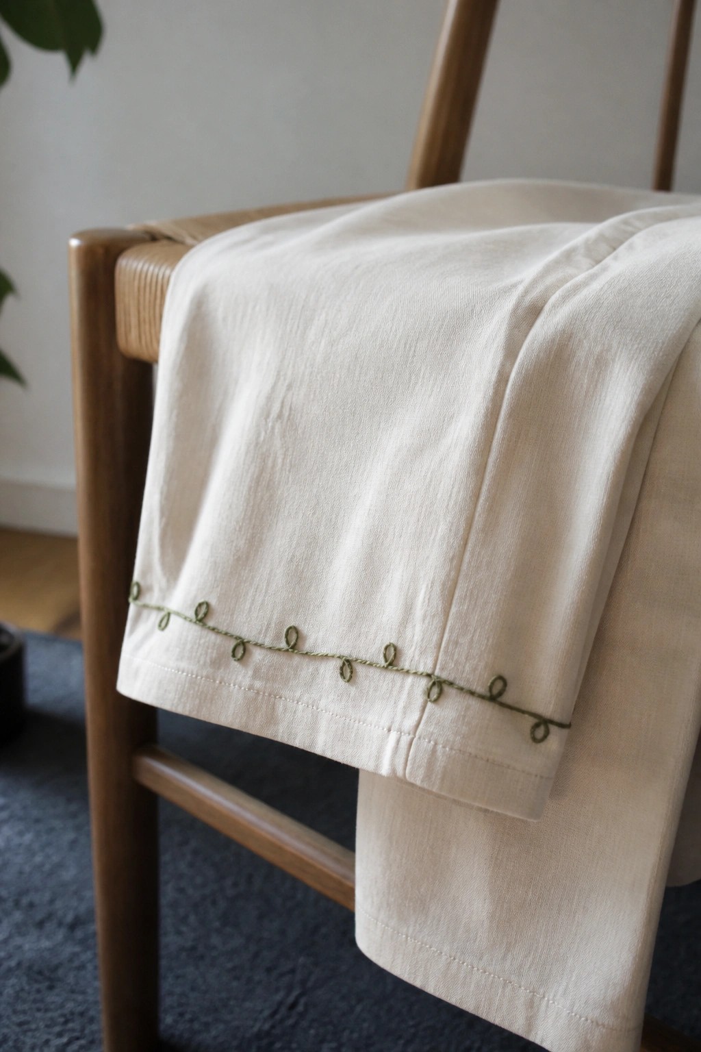 Cream fabric with a line of small green oval loops embroidered along the hem, draped over a wooden chair.