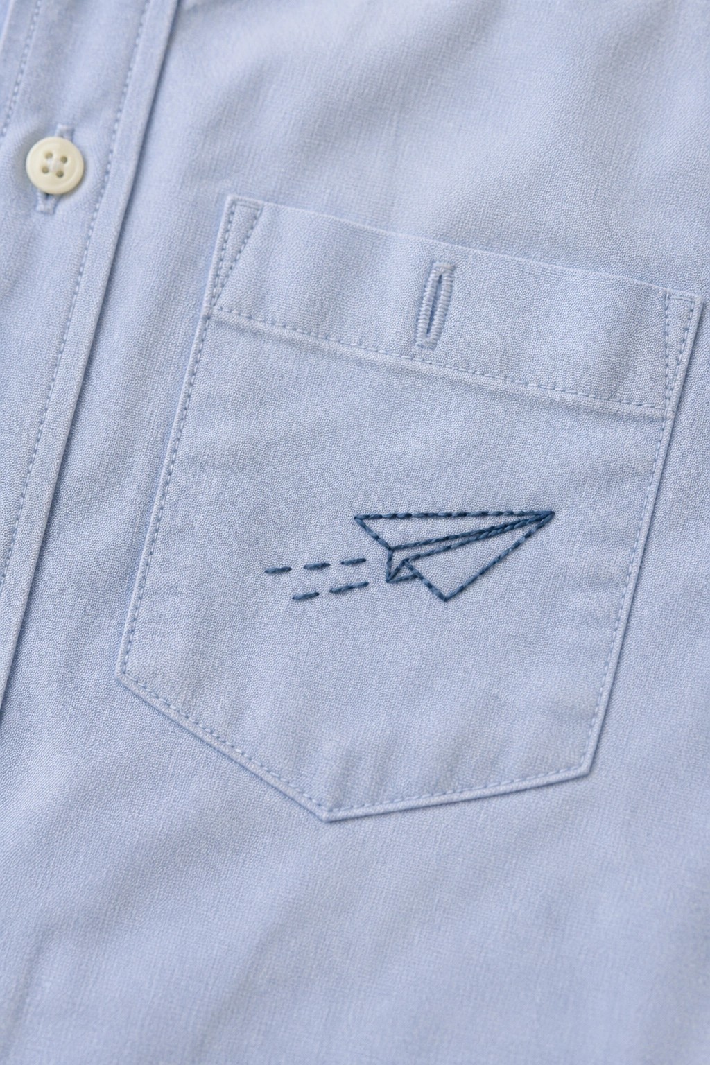 Light blue shirt pocket embroidered with paper airplane and dashed flight lines