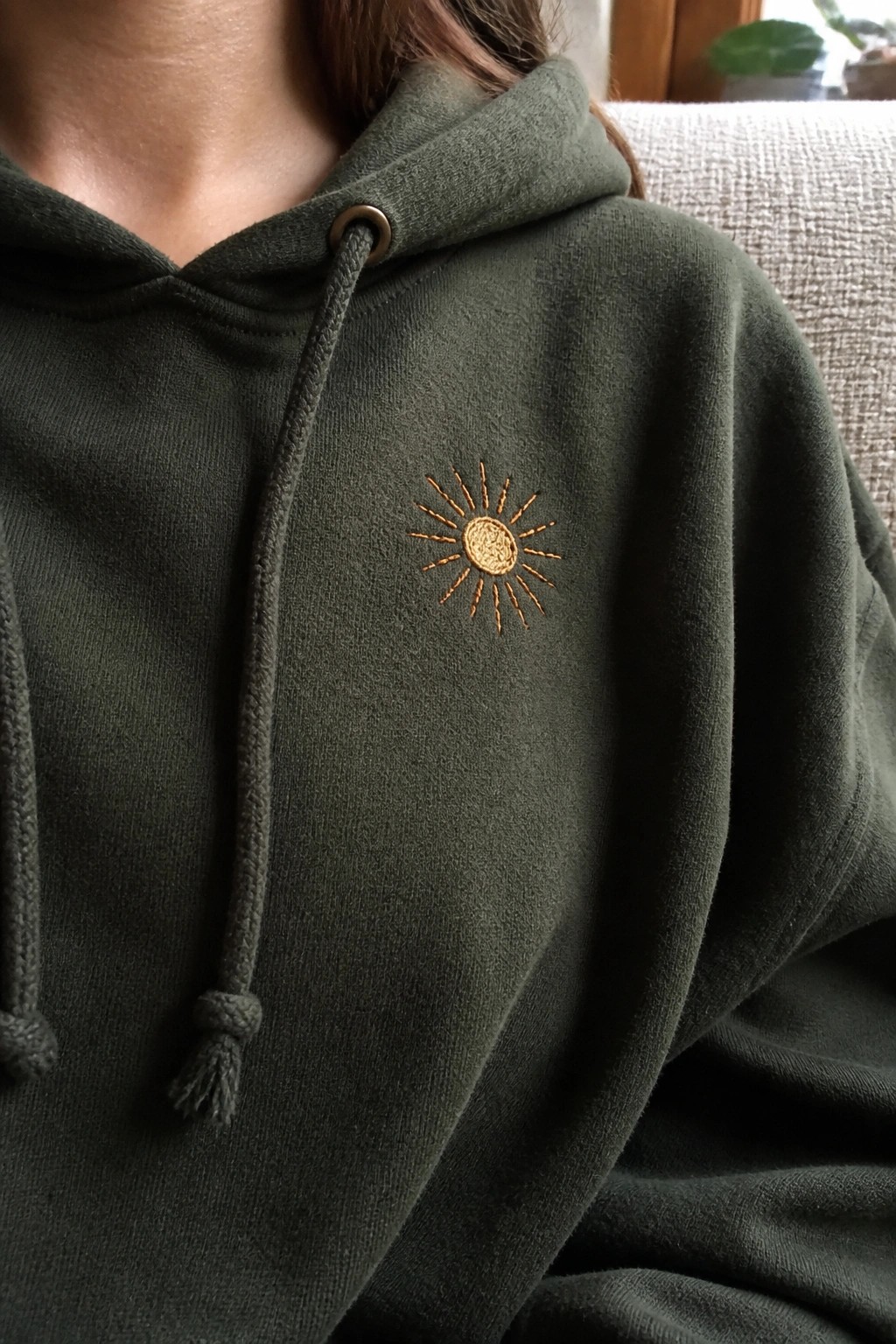 Dark green hoodie with small golden sun embroidery on the chest