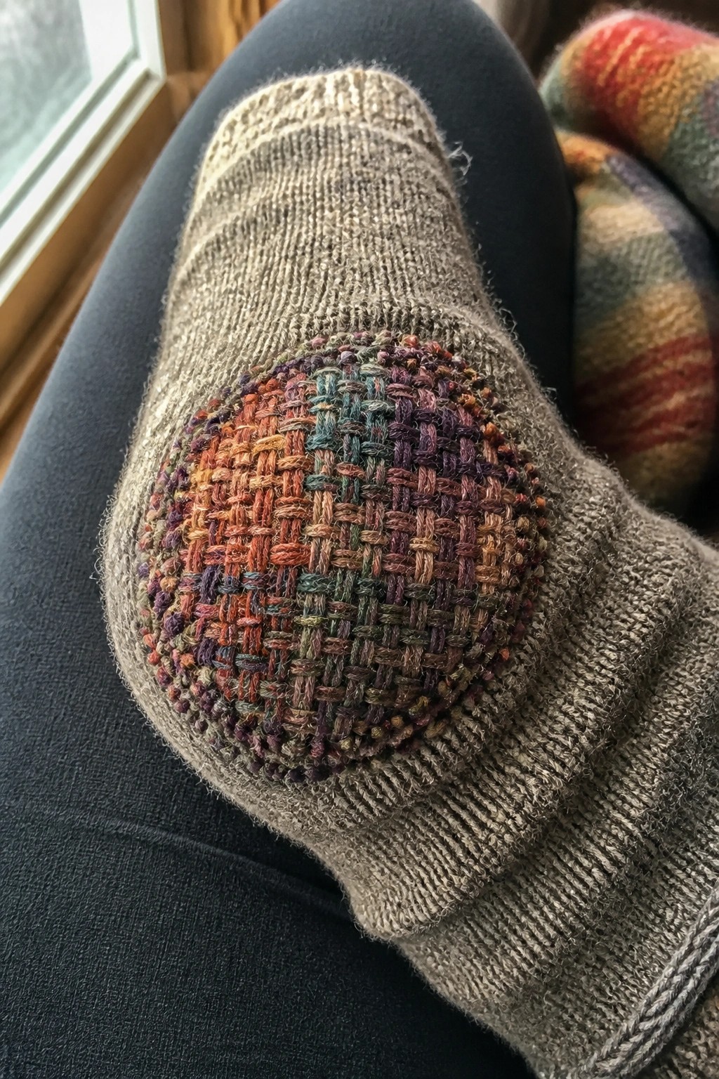 Gray sock with vibrant woven patch on bent knee, black leggings visible