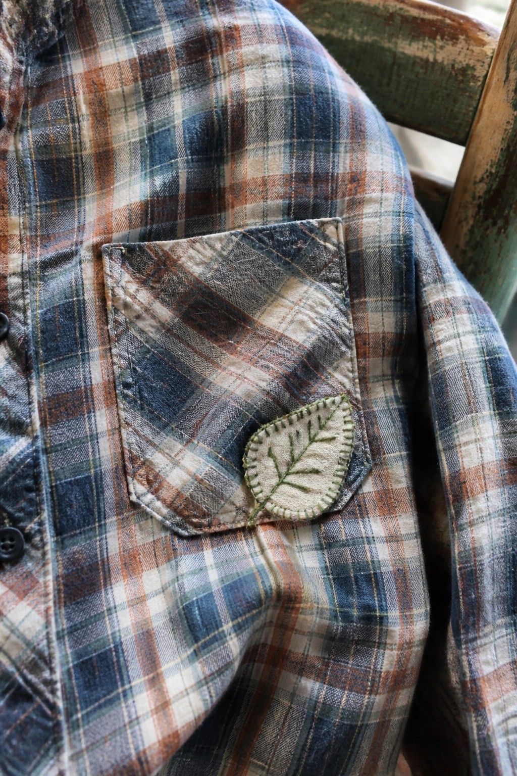 Blue and orange plaid flannel shirt with green embroidered leaf on pocket.