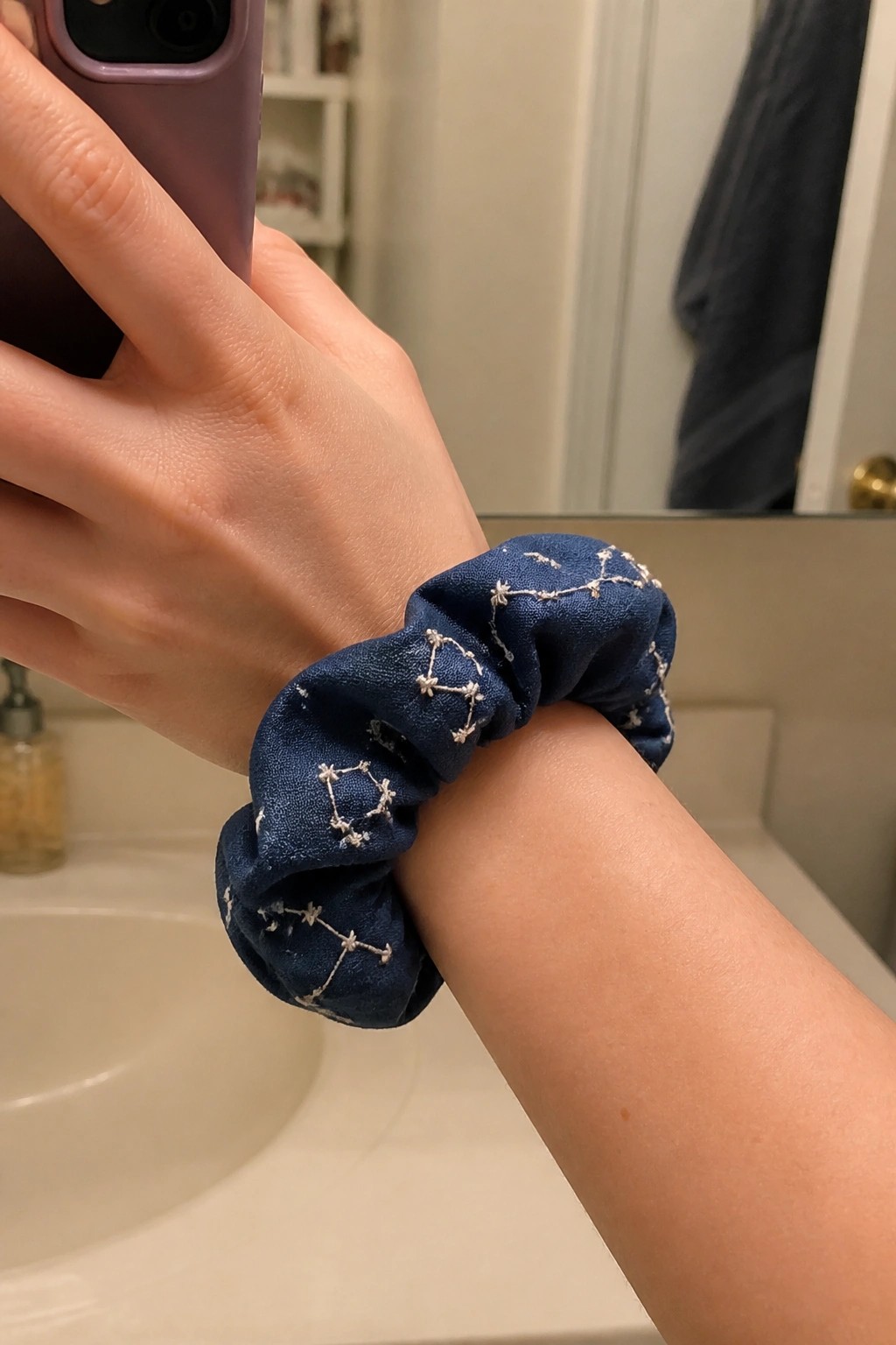 Hand holding purple phone, blue scrunchie with white constellation embroidery on wrist