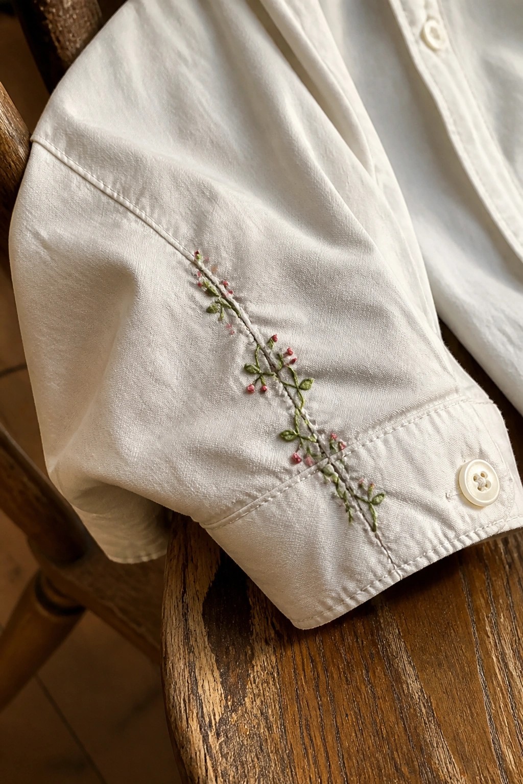 White shirt cuff with green vine and pink floral embroidery on wood