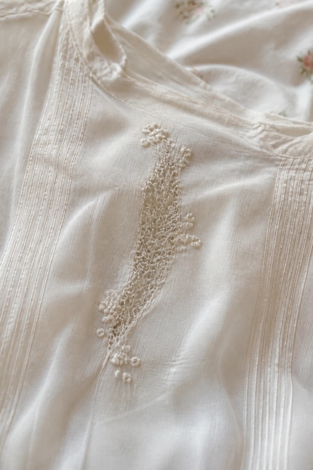 White fabric with delicate lace embroidery, floral motifs, and pleated seams.