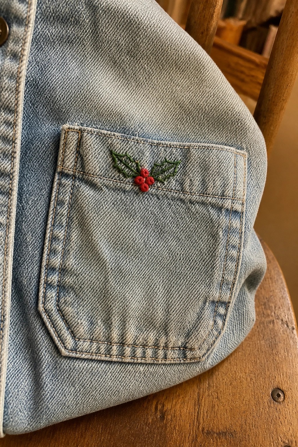 Light blue denim jacket pocket embroidered with holly leaves and red berries.