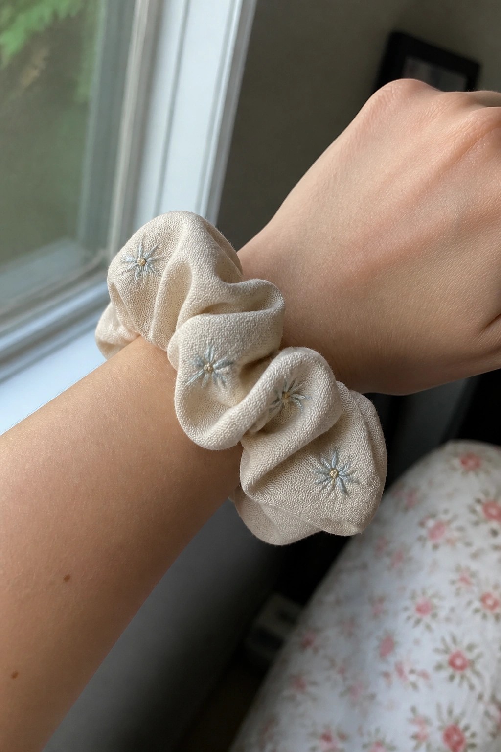 Beige scrunchie with embroidered blue stars on a wrist by a window