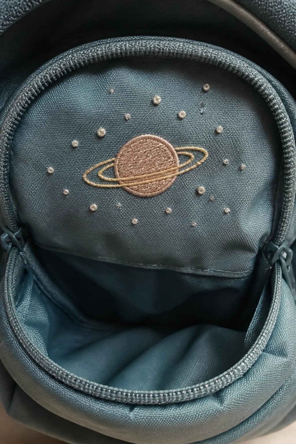 Open teal bag interior with embroidered brown Saturn planet and starry dots on fabric