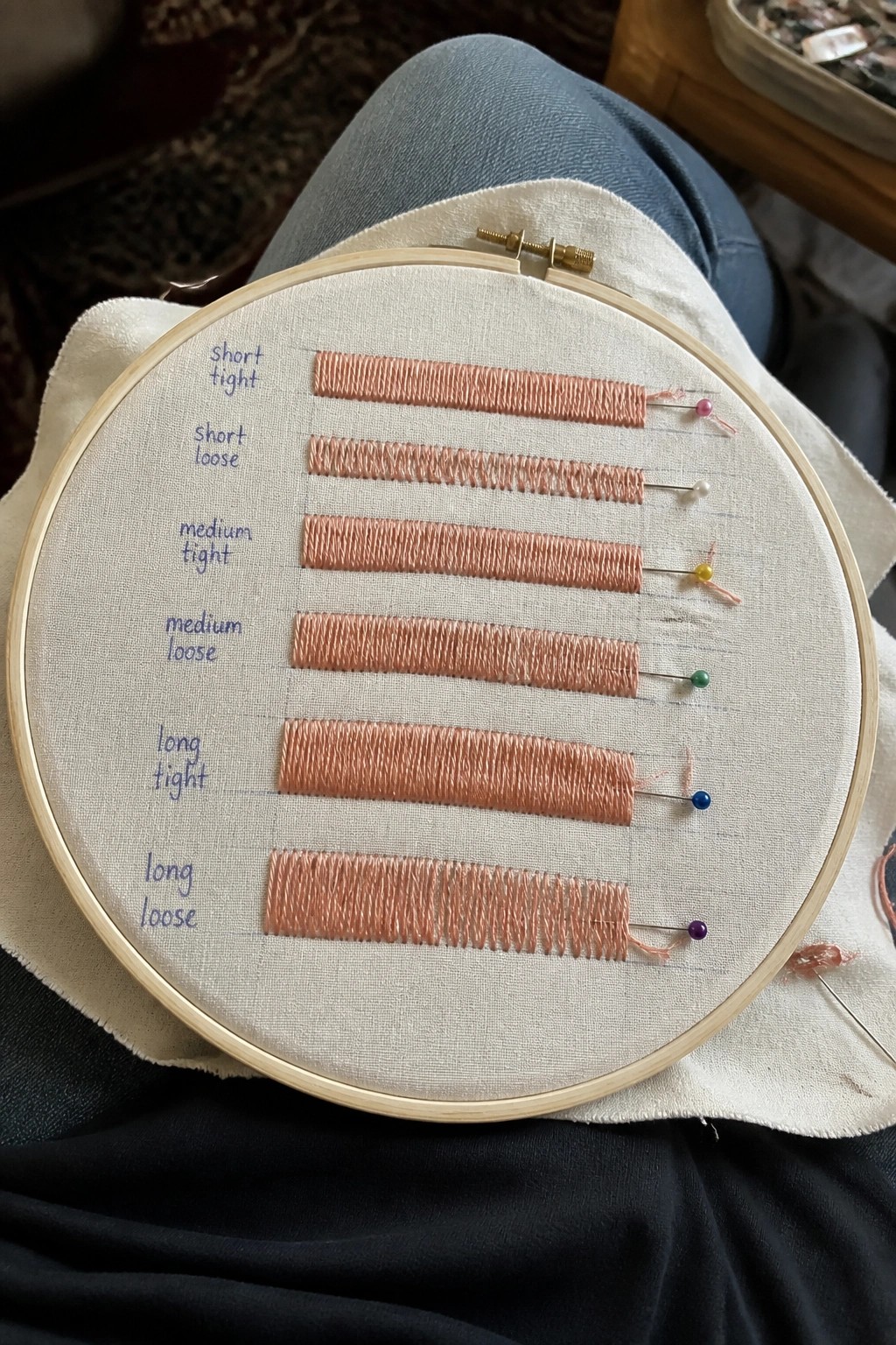 Wooden hoop on lap holds labeled peach stitches from short tight to long loose.