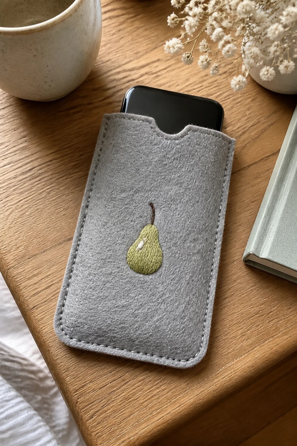 Gray felt phone sleeve with embroidered green pear on wooden table