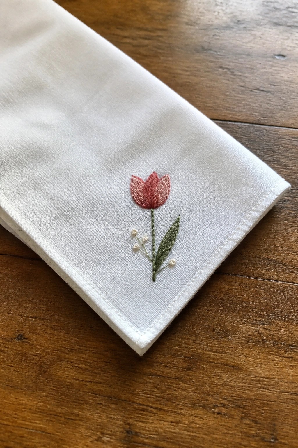 Pink tulip embroidery with green leaf and white buds on white fabric.