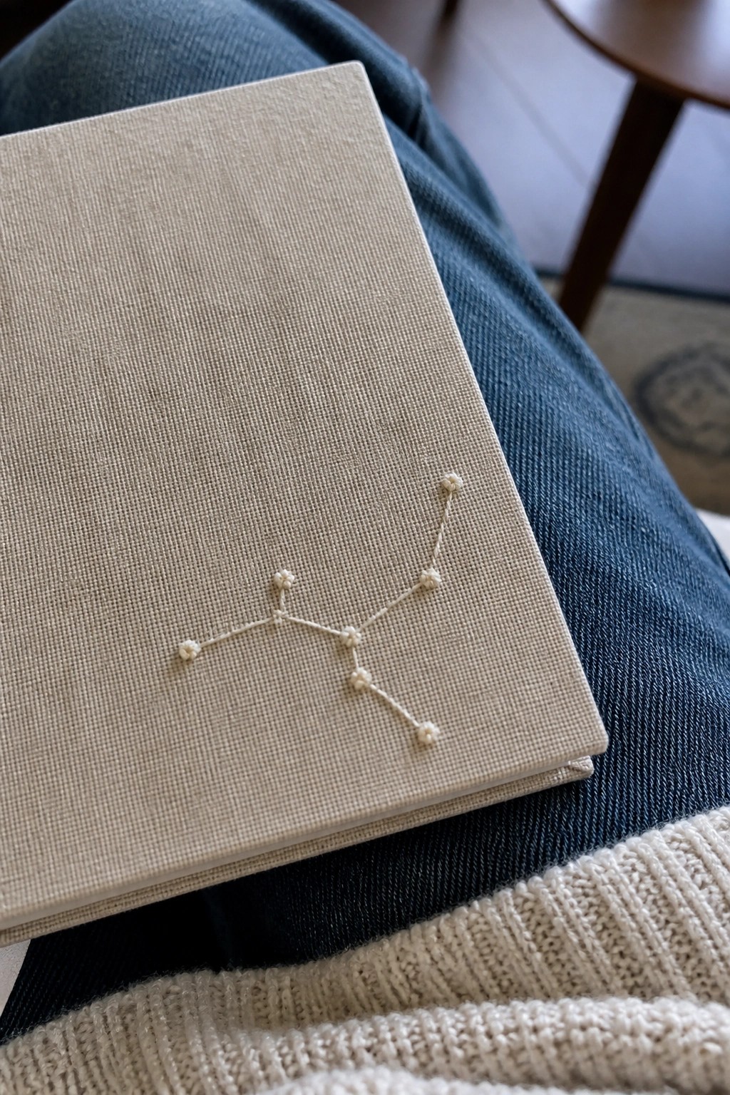 Beige embroidered constellation notebook on blue denim jeans with cream sweater