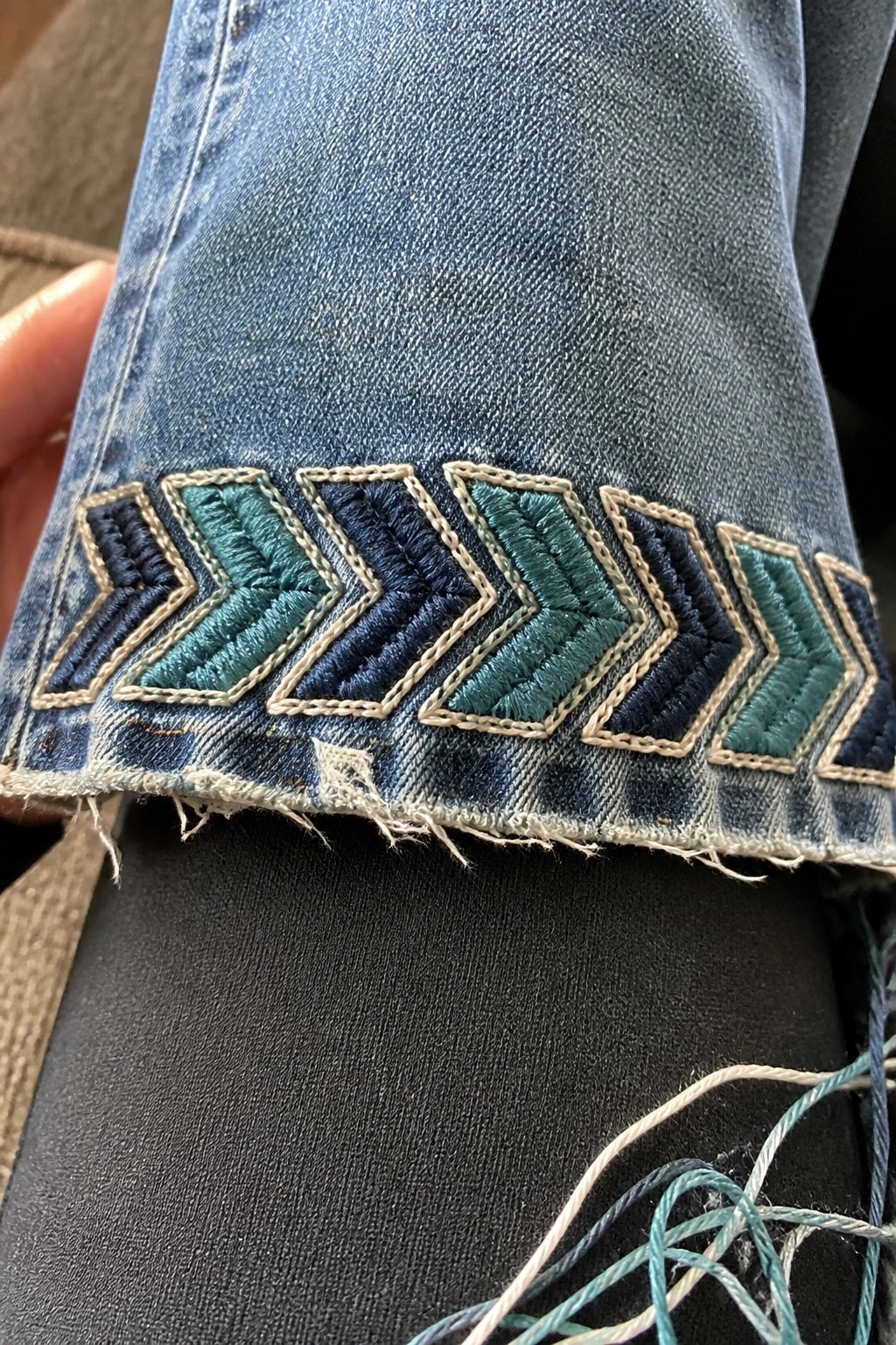 Blue denim jeans cuff with teal and navy chevron embroidery on frayed hem