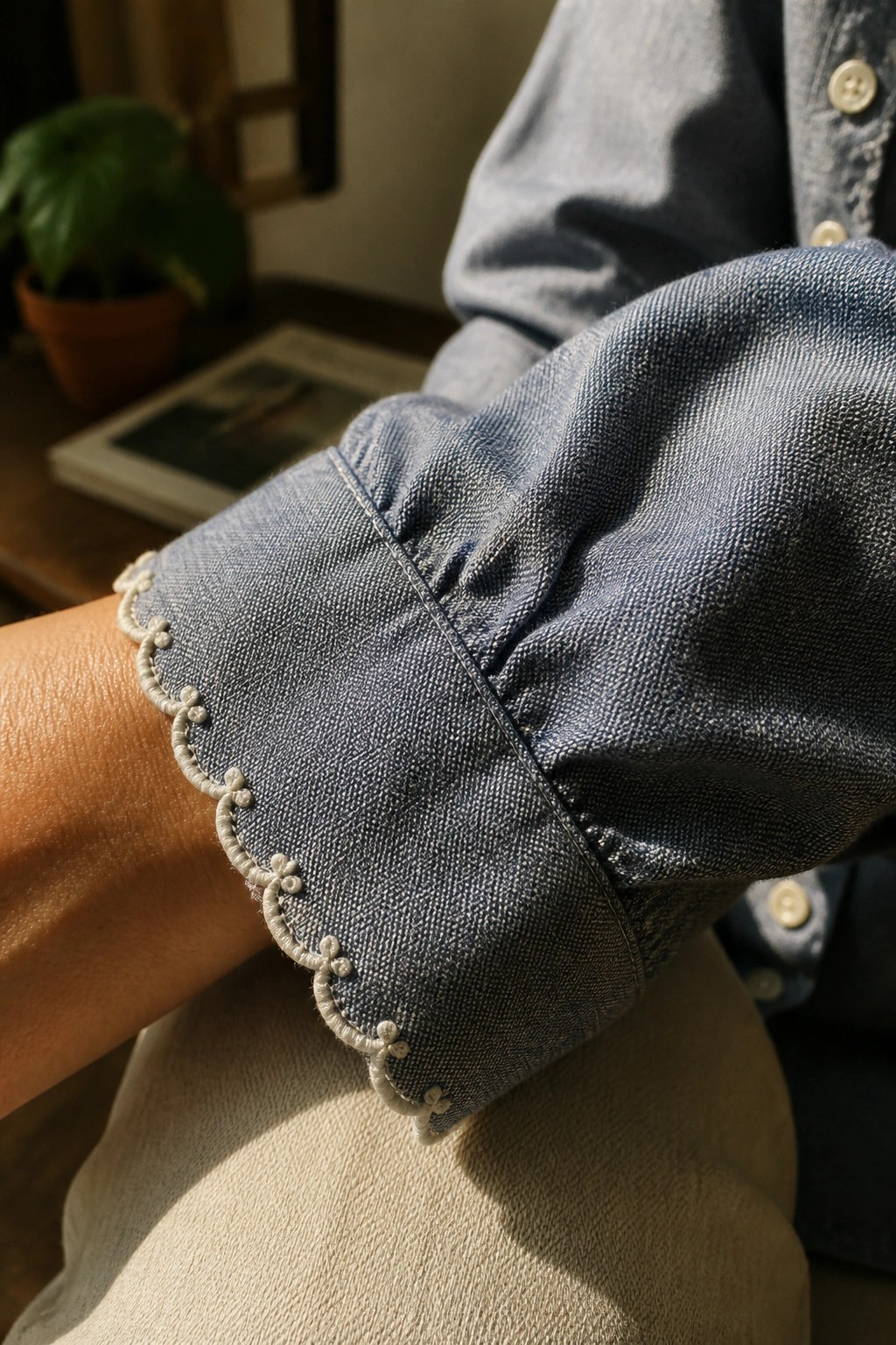 Close-up of a blue denim shirt cuff with light thread scalloped embroidery along the edge.