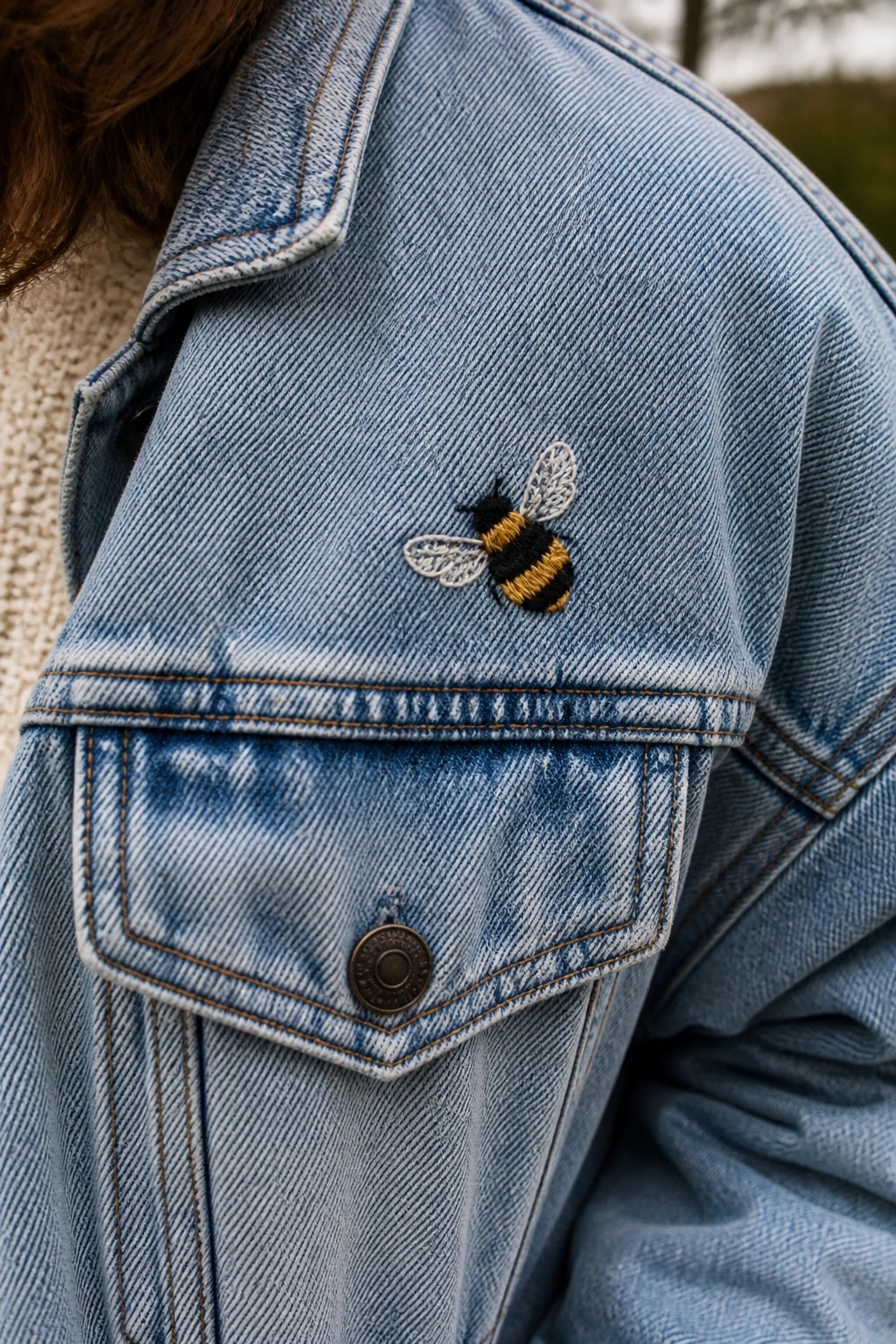 Embroidered bumblebee on shoulder of light blue denim jacket above pocket