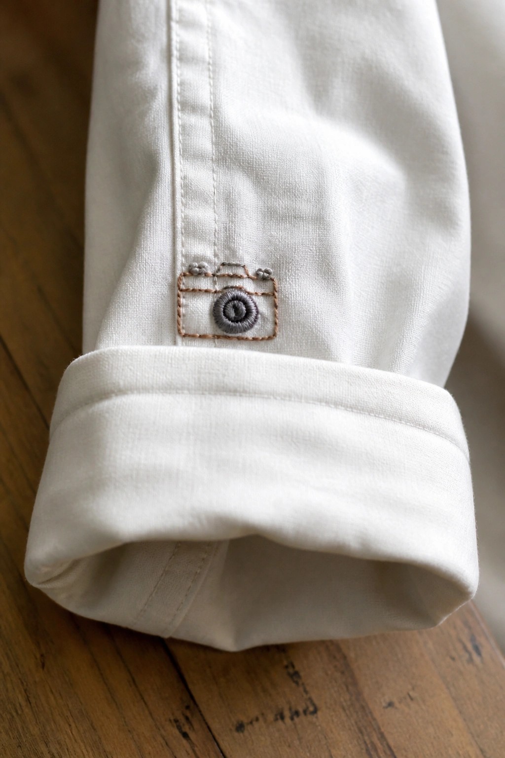 White fabric cuff with brown and gray embroidered camera on wood surface