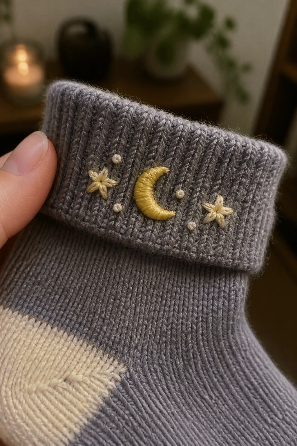 Hand holding gray knitted sock with yellow moon and star embroidery on cuff