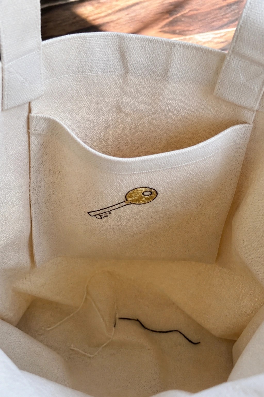 White canvas tote interior with gold embroidered key on inner pocket